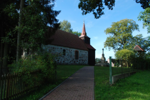 Kamienny kościół wśród drzew, po prawej pomnik